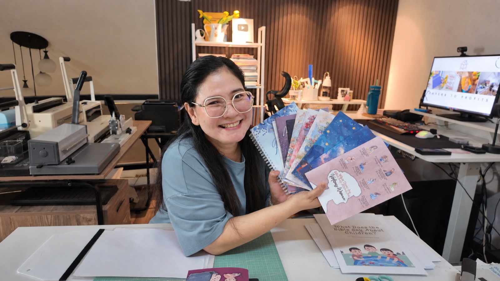 Grace, founder of Print Gracefully, holding a fan of handmade journals in her workshop